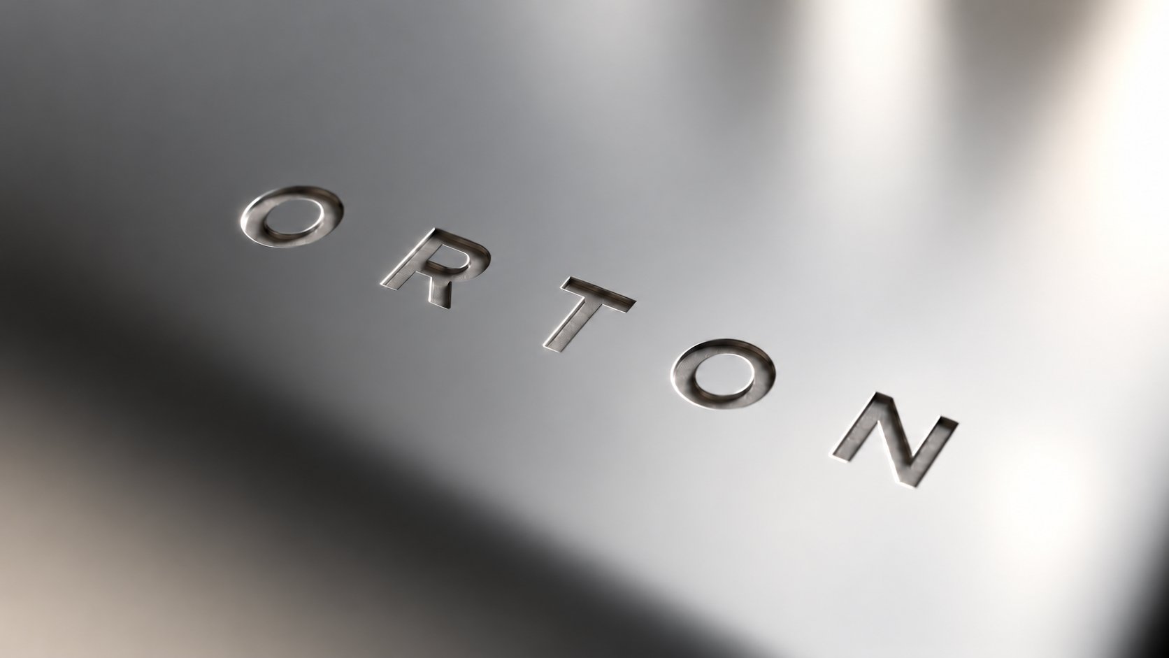 The ORTON wordmark engraved into polished metal, catching the light.
