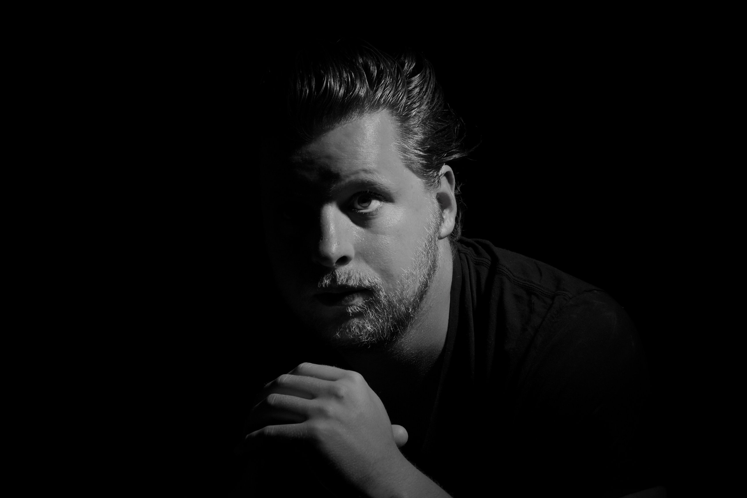 Black and white portrait of Tom Ritson, lit from one side against a dark background.